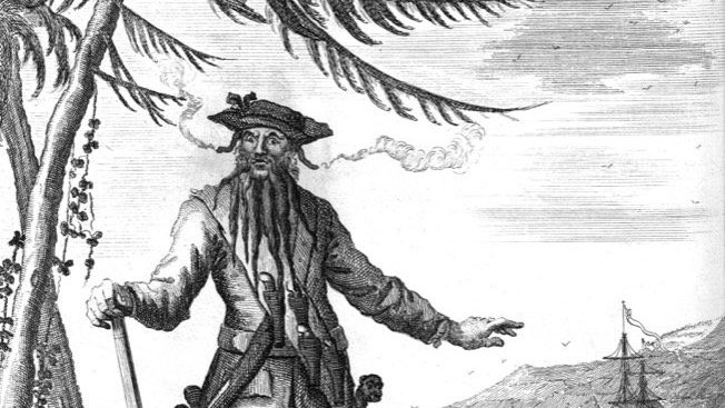 18th-century engraving of Edward Teach, known as Blackbeard, standing on a wharf armed with swords and a bandoleer of pistols