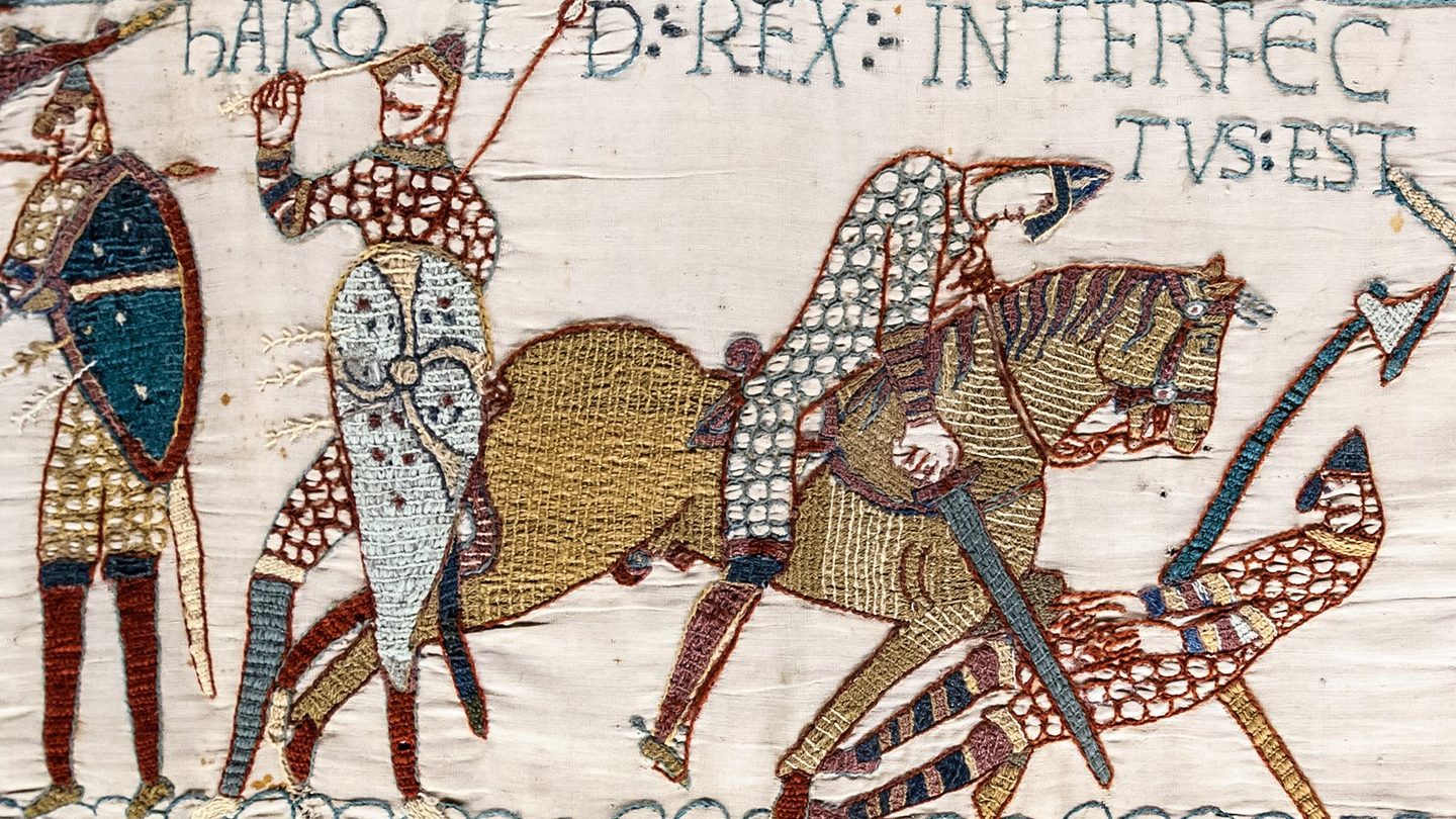 Bayeux Tapestry scene 57 showing a mail-clad figure raising a hand that holds a shaft beside a mounted Norman cutting down a fallen man, under the words HAROLD REX INTERFECTUS EST