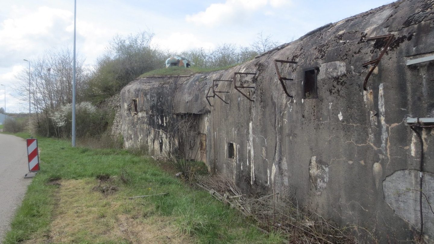 Photograph of the weathered concrete facade of Fort Casso, a Maginot Line fortress near Rohrbach-lès-Bitche, France, showing its gun embrasures and rusted anti-shell rail deflectors