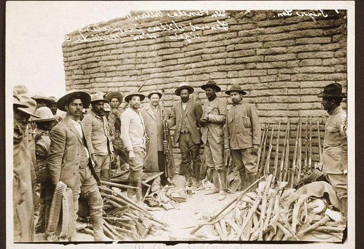 Circa-1914 photograph of Pancho Villa posed with Mutual Film Corporation photographer Carl von Hoffman, an interpreter, Colonel Trinidad Rodríguez, and other men in front of a pile of captured rifles