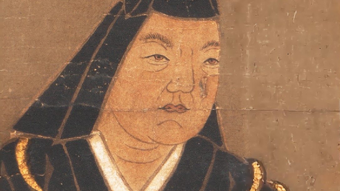 Cropped detail of a Rinsen-ji Temple portrait of Uesugi Kenshin in a black hood and robe, seen from the front with a lined, heavy-set face